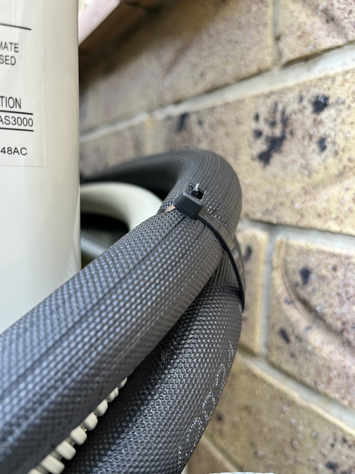 Black UV-rated cable tie securing insulated air conditioning pipework