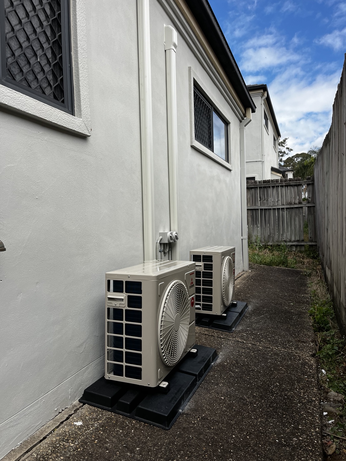 Two Mitsubishi Electric outdoor units grouped along the side of a customer's home by Swind